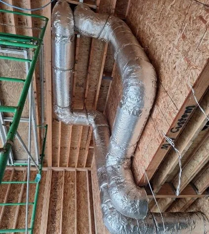 Insulated flexible HVAC ducts routed through unfinished wood framing with a laminated beam marked Custom