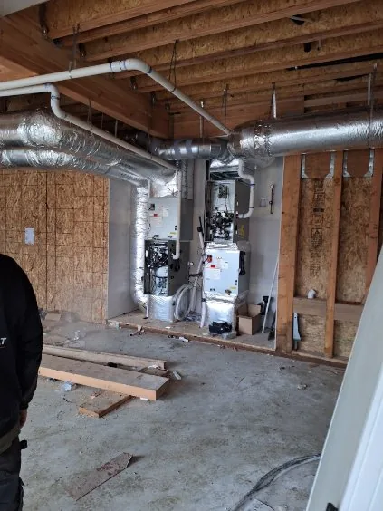 Dual furnace or air handler units with open service panels, insulated ducts, and PVC lines in unfinished framing