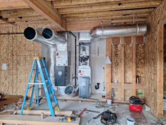 Dual HVAC units with open panels, blue stepladder, gas lines, and tools on a residential rough-in