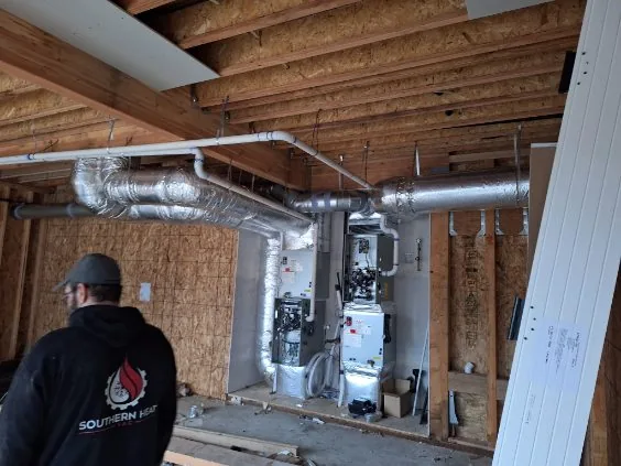 Southern Heat HVAC technician in branded hoodie facing dual open-panel units on a jobsite
